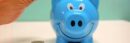 Hand inserting a coin into a blue piggy bank for savings and money management.